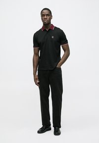 Svart polotrøye med rød kant, korte ermer og en logo på brystet. Kombinert med svarte bukser og svarte sko. Enkel design.