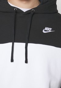 Sudadera con capucha Nike en blanco y negro, con cordones negros y el logo de Nike en el pecho superior, llevada sobre una camiseta blanca.