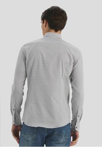 Chemise à carreaux gris et blanc avec col boutonné, manches longues et accents de boutons, associée à un jean denim bleu.