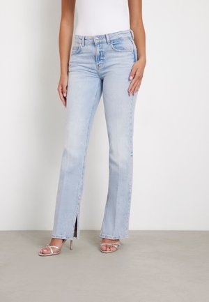 Jeans a palazzo azzurri chiari con fenditure frontali, realizzati in denim. Presentano un classico design a cinque tasche e una chiusura con bottone. Abbinati a tacchi a stiletto argento.