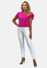Fuksjowa bluzka z falbaniastymi rękawami, w zestawie z białymi dopasowanymi spodniami i wysokimi obcasami w wężowy wzór. Gładki materiał o eleganckim wyglądzie.