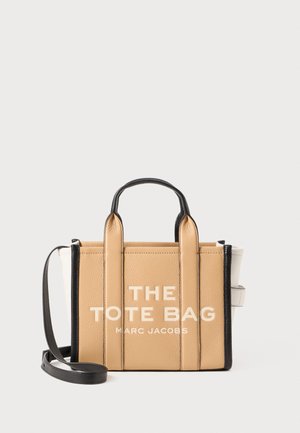 Tan leather tote bag with black accents and straps, featuring embossed text "THE TOTE BAG MARC JACOBS." Compact rectangular shape.