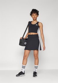 Top corto atletico nero e gonna con strisce bianche, sneakers nere e calze a righe. Include una borsa sportiva nera.