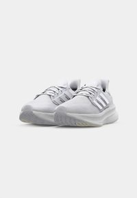 Weiße Sportschuhe mit einer strukturierten Oberseite, drei auffälligen Streifen an den Seiten und einer gepolsterten Sohle mit einem Profilmuster.