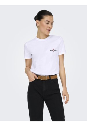 Mujer con cabello oscuro recogido en un moño, vistiendo una camiseta blanca con el texto "AMOUR", pantalones negros y un cinturón marrón, mirando ligeramente hacia su derecha.