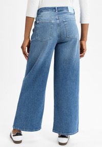 wijdvallende blauwe denim jeans met een hoge taille, voorzien van achterzakken en een subtiele textuur. Gecombineerd met witte sneakers voor contrast.
