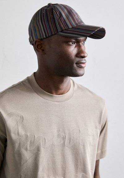 Beige T-skjorte med preget tekst, kombinert med en caps med flerfargede vertikale striper. Capsen har en bøyd skygge og ventilasjonsluker.