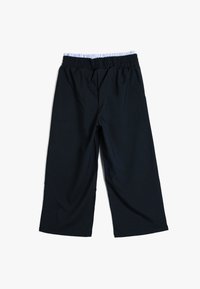 Schwarze weit geschnittene Hose aus weichem Stoff mit einem elastischen Bund, der ein hellblau-weiß gestreiftes Innenfutter aufweist.