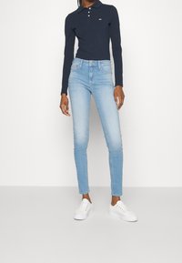 Schmale Jeans aus hellblauem Denim, kombiniert mit einem navyblauen Langarm-Polo und weißen Sneakers. Mit einem figurschmeichelnden Schnitt und schlichten Nähten.