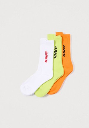 Three pairs of crew socks: white with red logo, green with black logo, and orange with black logo. Ribbed texture, cotton blend material.