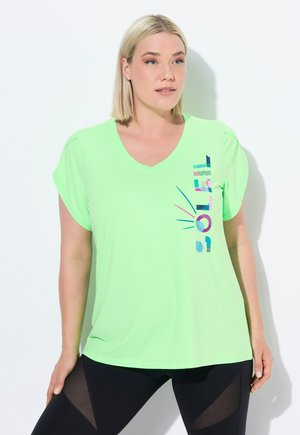 Světle zelené sportovní tričko, design do V, krátké ohrnuté rukávy, na boku s vícbarevným grafickým textem, kombinované s černými legínami.