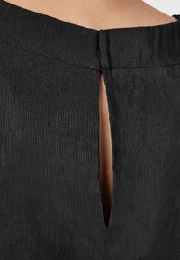 Svart tyg med en subtil lyster, med en slits bak med en ren kant och en texturerad yta. Minimalistiska designelement.