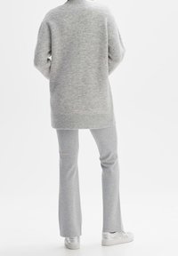 Šedý pletený svetr s dlouhými rukávy, v oversized střihu; doplněný o světle šedé rozšířené kalhoty. Obuv tvoří lesklé stříbrné tenisky.