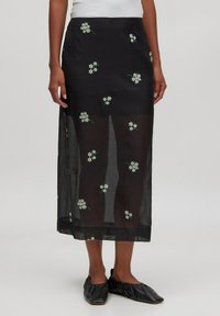 Schwarzer, transparenter Rock mit weißen Blumenstickereien und grünen Akzenten, mittellanges Design mit leichtem Material.