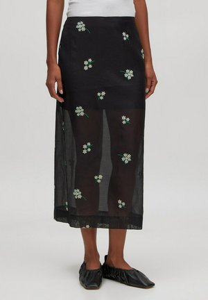 Schwarzer, transparenter Rock mit weißen Blumenstickereien und grünen Akzenten, mittellanges Design mit leichtem Material.