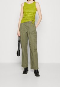 Débardeur côtelé vert citron avec détail de cordon de serrage latéral, associé à un pantalon cargo à jambes larges vert olive avec poches, porté avec des bottines noires.