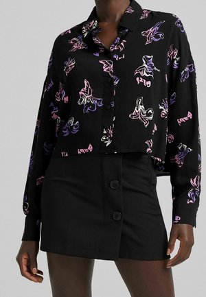 Black cropped button-up shirt with colorful butterfly patterns, paired with a black skirt featuring two dark buttons at the front.