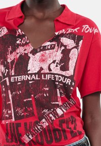 T-shirt en coton rouge avec un décolleté en V profond, des manches courtes et une impression graphique avec du texte et des images en noir et blanc.