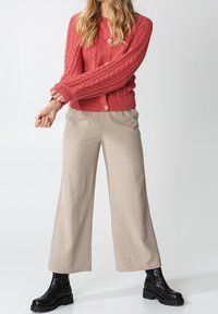 Koral färgad kabelstickad cardigan med runt knappar, parat med beige vida byxor och svarta ankelstövlar. Släta texturer och avslappnad passform.