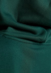 Tela de algodón verde oscuro con una textura suave, que presenta pliegues que crean una apariencia en capas. La costura visible añade detalle.