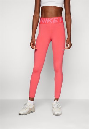 Leggings rosa con una fascia larga in vita che presenta il marchio "NIKE" in bianco. Tessuto liscio e elasticizzato con un design aderente. Indossati con sneakers bianche.