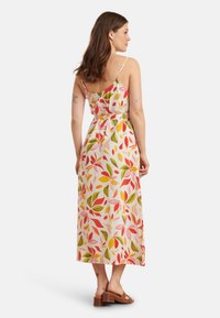 Florales Maxikleid mit dünnen Trägern, das einen weißen Grund und lebendige rote, grüne und gelbe Blattmuster aufweist. Es endet knapp unter den Knöcheln.