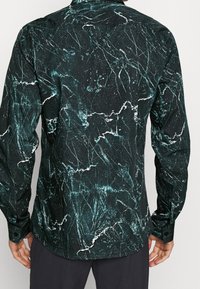 Camicia nera con motivo marmorizzato verde e bianco, maniche lunghe, polsini con bottone, colletto e una finitura del tessuto testurizzata.