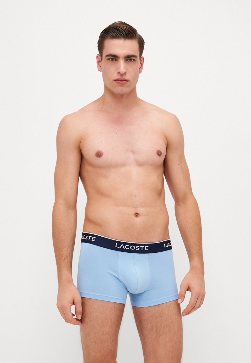 Boxer briefs de color azul claro con una cinturilla en color marino que presenta el logo de Lacoste. Tela suave, forma ajustada, largo por encima del muslo y sin patrones.