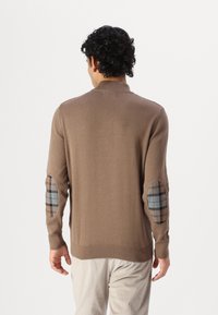 Pull en tricot marron avec col côtelé, doté de coudières en plaid beige. Texture douce, coupe ajustée et manches longues.