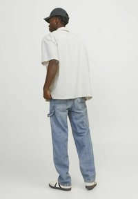 Lysfarvet kortærmet skjorte og blå baggy jeans. Skjorten har en krave og er løs i pasformen. Outfittet suppleres med en mørk kasket.