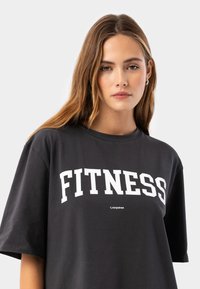 Black oversized t-shirt made of cotton, featuring bold white "FITNESS" text and short sleeves, with a smooth texture and relaxed fit.