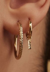 Gold hoop earrings featuring a textured design and a small dangling accent, showing a polished finish and geometric patterns.