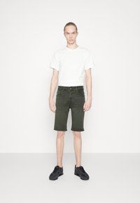 Witte katoenen t-shirt, olijfgroene denim shorts en zwarte sportschoenen. Rechte pasvorm met een knielange snit en minimale details.