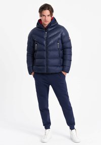 Marinblå pufferjacka med huva, med quiltat mönster och dragkedjefickor. Matchad med marinblå joggers och vita hög-top sneakers.