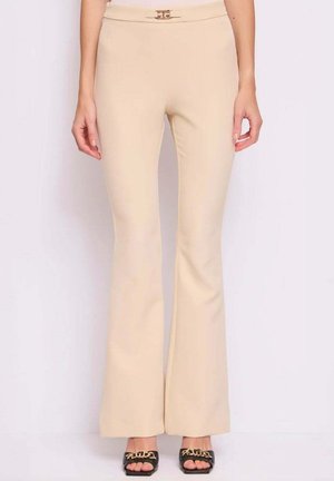 Donna che indossa pantaloni beige a vita alta svasati con una piccola cintura con fibbia e tacchi neri open-toe con dettaglio a catena dorata.