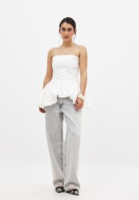 Top blanco sin tirantes con un dobladillo con volantes, combinado con unos jeans de pierna ancha gris claro de cintura alta. Zapatos y accesorios a rayas en blanco y negro.