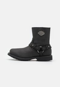 Bota de cuero negro hasta el tobillo con punta redonda, detalle de correa, acento de anillo de metal y marca Harley-Davidson en el lateral. Suela de goma.