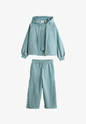 Šviesiai mėlynas trijų dalių laisvalaikio kostiumas su gobtuvu ir užtrauktukine striuke, trumpomis rankovėmis palaidine ir elastingomis juosmens kelnėmis su raišteliu bei šonine užrašo detalė.