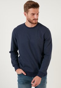 Námornícky modré mikina vyrobená z mäkkého materiálu, s okrúhlym výstrihom a rebrovanými manžetami a spodným lemom. Jemná textúra po celom materiáli.