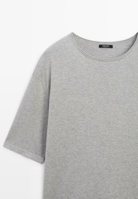 Jasnoszary, krótki rękaw, bawełniany t-shirt z okrągłym dekoltem i widoczną czarną metką wewnątrz kołnierza.