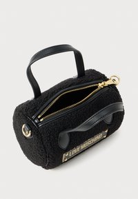 Borsa a mano nera in peluche con accenti in pelle, di forma rotonda, con zip dorata e patch con logo. Presenta manici corti per una facile portabilità.