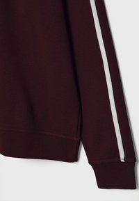 Manche de sweat-shirt marron avec une bande blanche unique courant verticalement le long du bras, montrant les détails des poignets et de l'ourlet côtelés.