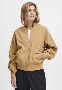 Hnedá bomber bunda vyrobená z hladkej tkaniny. Má predný zips, rebrované manžety a dve bočné vrecká. Jednoduchý dizajn bez viditeľných vzorov.