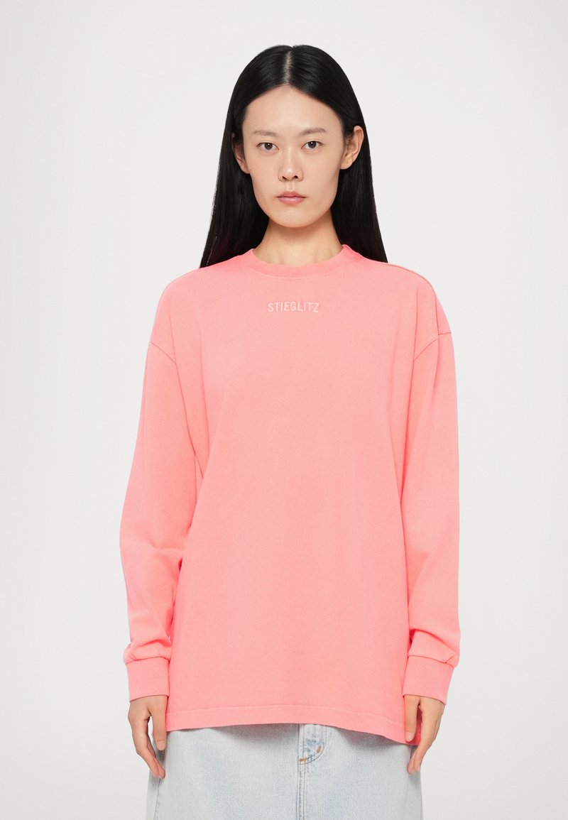 Oversized long-sleeve sweatshirt in bright pink cotton. Features crew neckline and "STIEGLITZ" printed on the chest in white.
