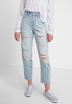 Jean déchiré bleu clair avec plusieurs patches usés, taille haute et coupe droite, associé à des baskets grises.