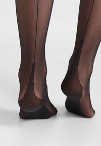 Černé průsvitné punčochy s texturovaným povrchem, s dekorativním švem na zadní straně a vyztuženou špičkou, zdůrazňující elegantní design.