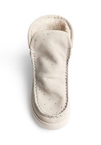 Zapatilla beige hecha de suave ante, con forro de piel sintética, adornos de strass y un acento cosido a lo largo del borde. Forma redondeada.