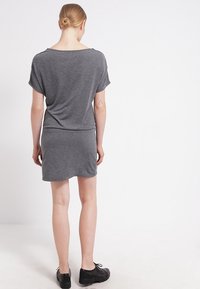 Szara sukienka z krótkim rękawem, luźny krój, elastyczny pas i prosty dół. Materiał wydaje się miękki i lekko strukturalny. Widać czarne buty.