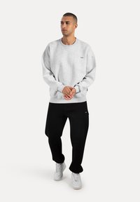 Grå sweatshirt med rund hals og ribbede manchetter, parret med sorte bukser og hvide sneakers. Sweatshirten har et lille logo detail.
