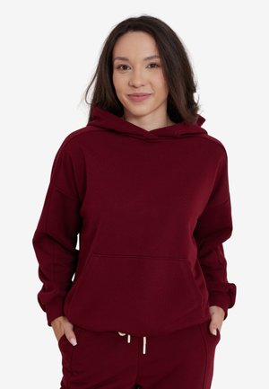 Burgundowa bluza z kapturem wykonana z miękkiej tkaniny, z przednią kieszenią kangurką, regulowanym kapturem na sznurku oraz luźnym krojem z prążkowanymi mankietami.
